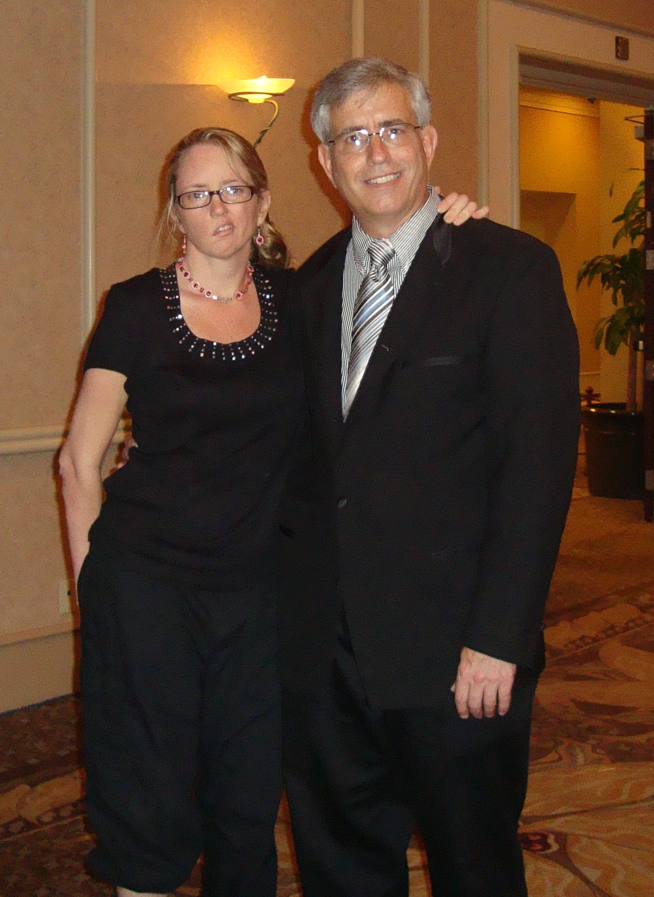 Cindy Reese dressed up in black pantsuit standing on left arm in arm with Bill Reese in suit standing on right
